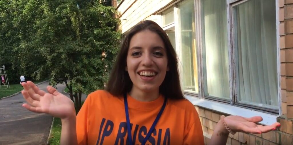 Участница языкового лагеря IP Russia на фоне деревьев у здания.